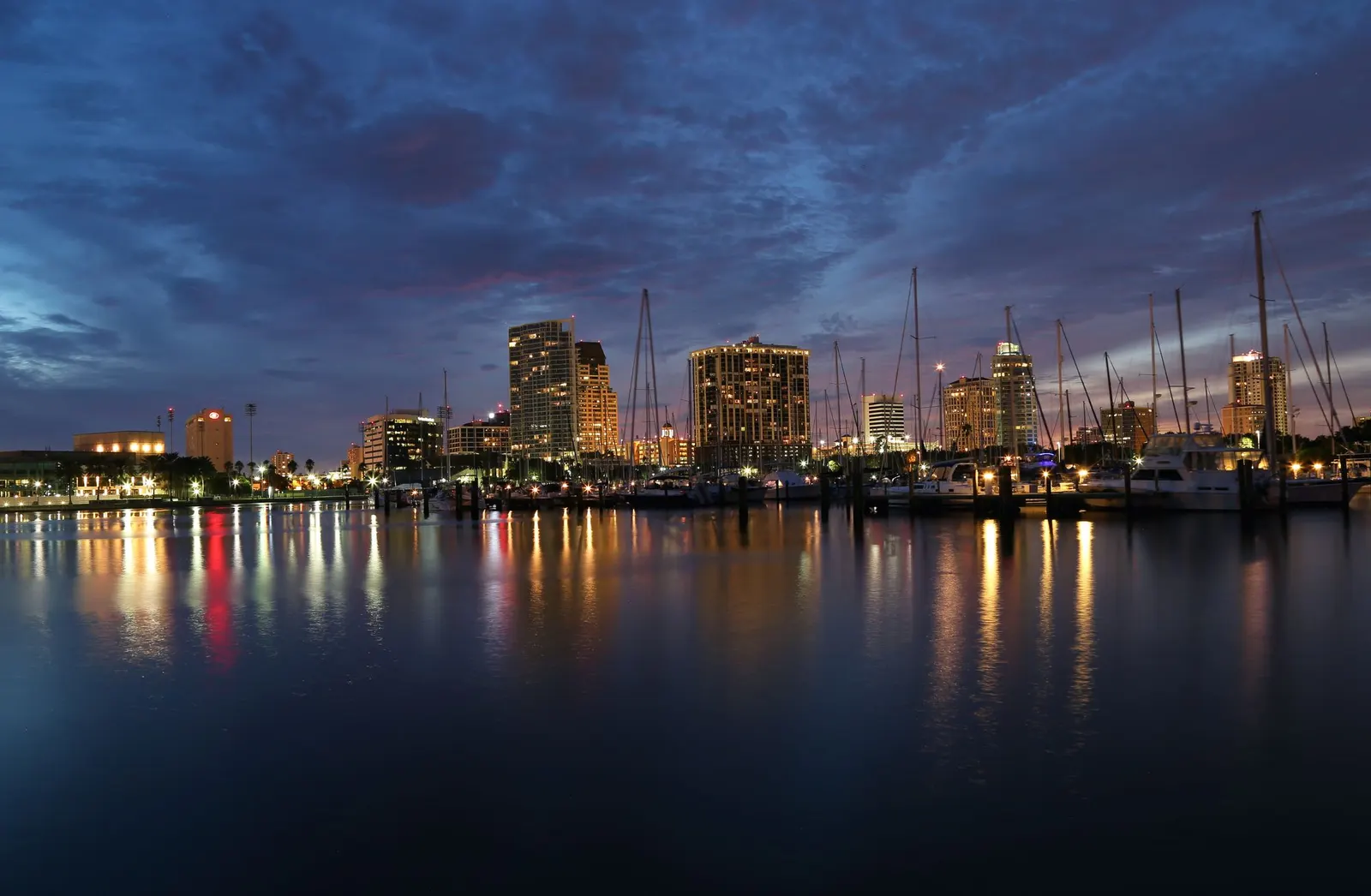 Marina with sailboats and a downtown skyline lit up at dusk