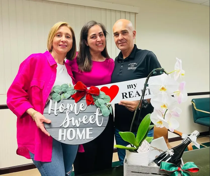 Gabriela with clients holding the Home Sweet Home sign, with an orchid and champagne on the table