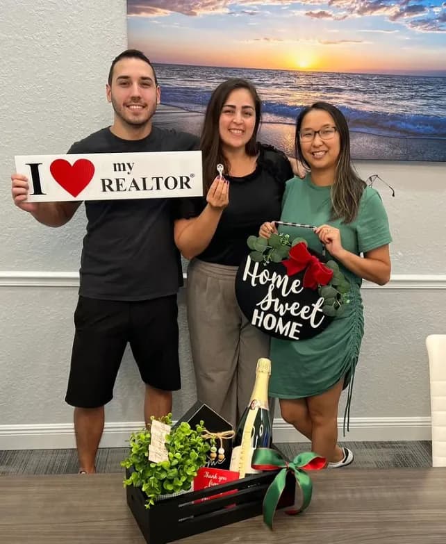 Clients with keys in hand and the Home Sweet Home sign in front of a beach painting