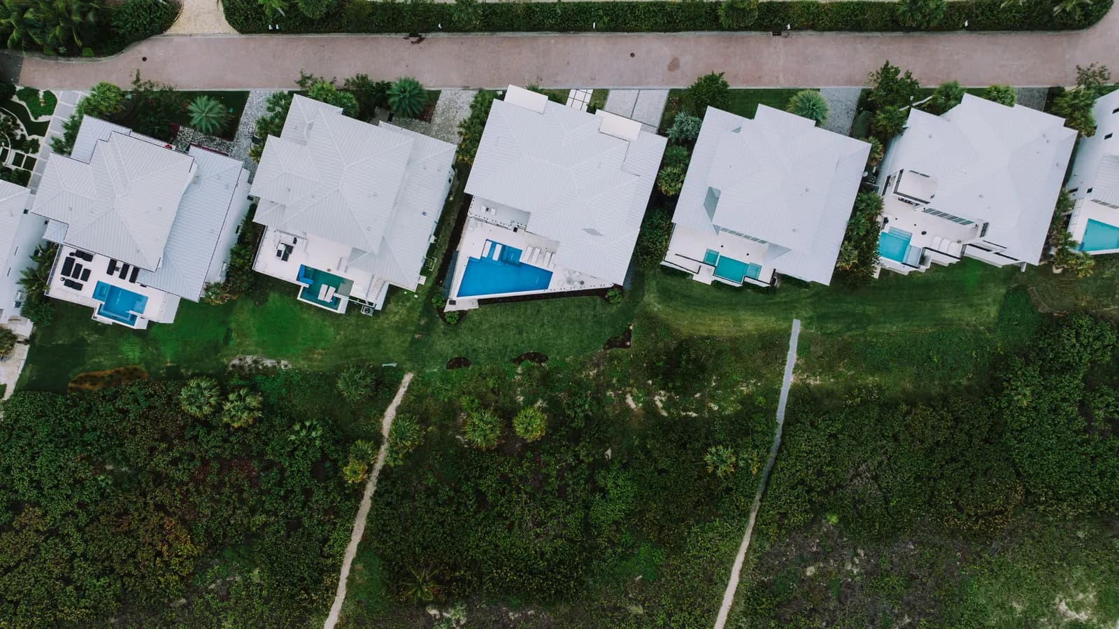Aerial view of a row of white houses with pools and green lawns
